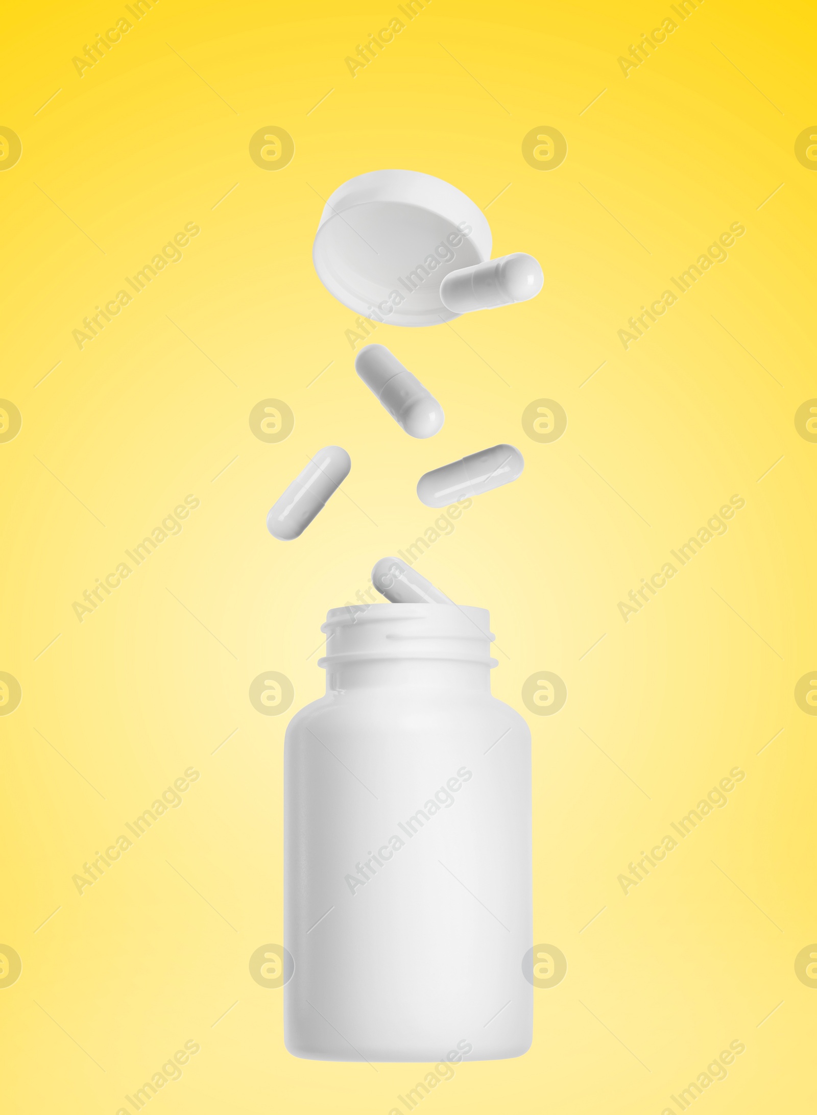 Image of Vitamin capsules falling into bottle on yellow background