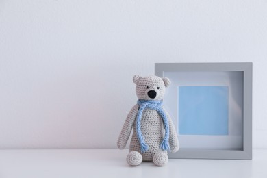 Photo of Empty photo frame and toy bear on table near white wall. Space for design