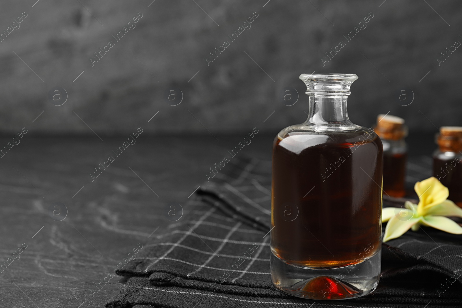 Photo of Aromatic homemade vanilla extract in glass bottle on table. Space for text