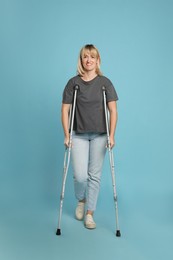 Full length portrait of woman with crutches on light blue background