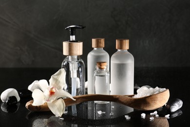Photo of Retreat concept. Bottles with cosmetic products, sea salt, spa stones and orchid flower on wet mirror surface