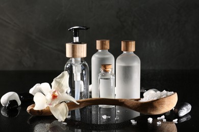 Retreat concept. Bottles with cosmetic products, sea salt, spa stones and orchid flower on wet mirror surface