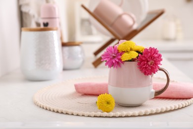 Photo of Beautiful bright flowers in cup on table indoors, space for text