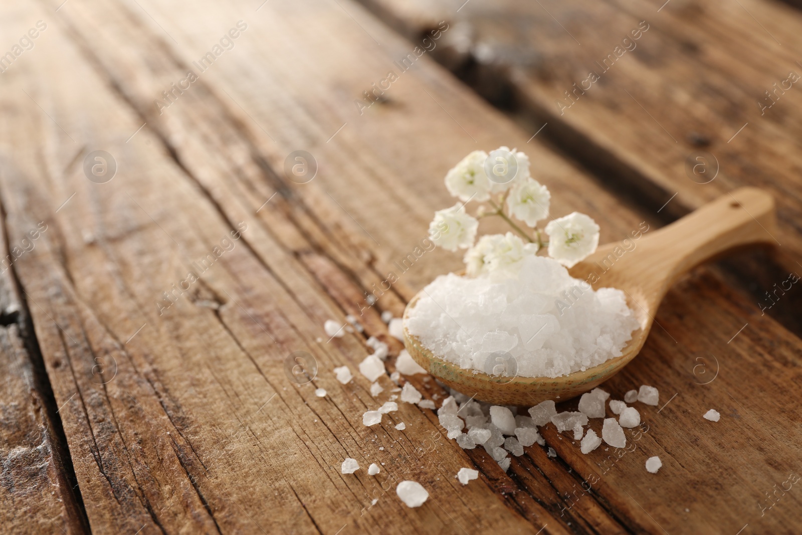 Photo of Aromatic sea salt and beautiful flowers on wooden table, closeup. Space for text