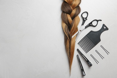 Photo of Flat lay composition with braid, hairdresser's tools and space for text on gray background