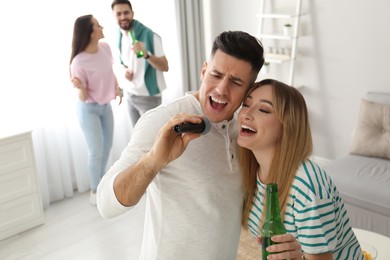 Happy couple singing karaoke with friends at home