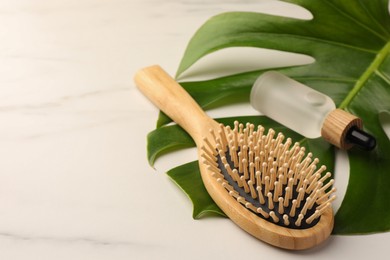 Wooden hair brush, bottle of essential oil and monstera leaf on white table
