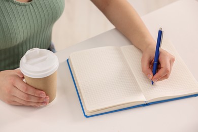 Photo of Young woman writing in notebook at white table, closeup