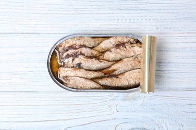 Tin can with conserved fish on wooden background, top view