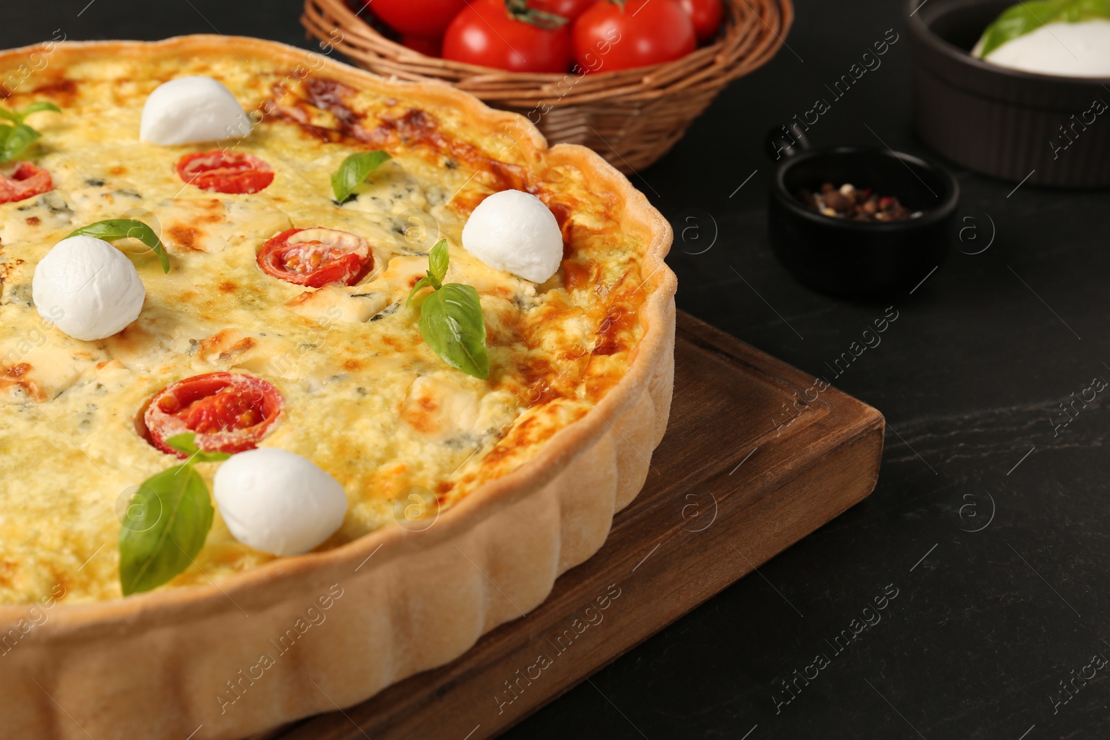 Photo of Delicious homemade cheese quiche and ingredients on black table, closeup