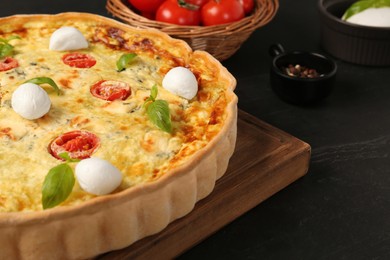 Photo of Delicious homemade cheese quiche and ingredients on black table, closeup