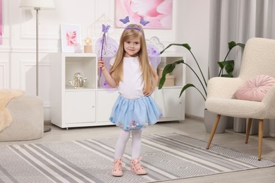 Cute little girl in fairy costume with violet wings and magic wand at home