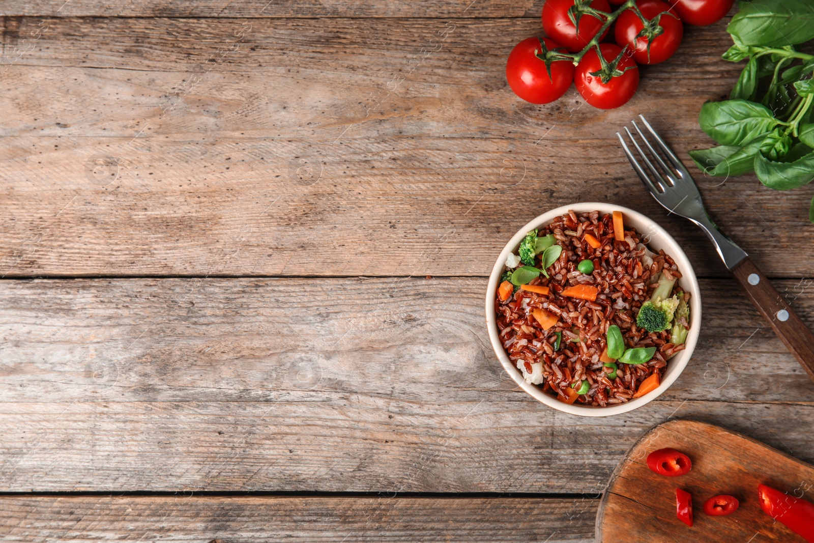 Photo of Bowl of brown rice with vegetables served on wooden table, flat lay. Space for text