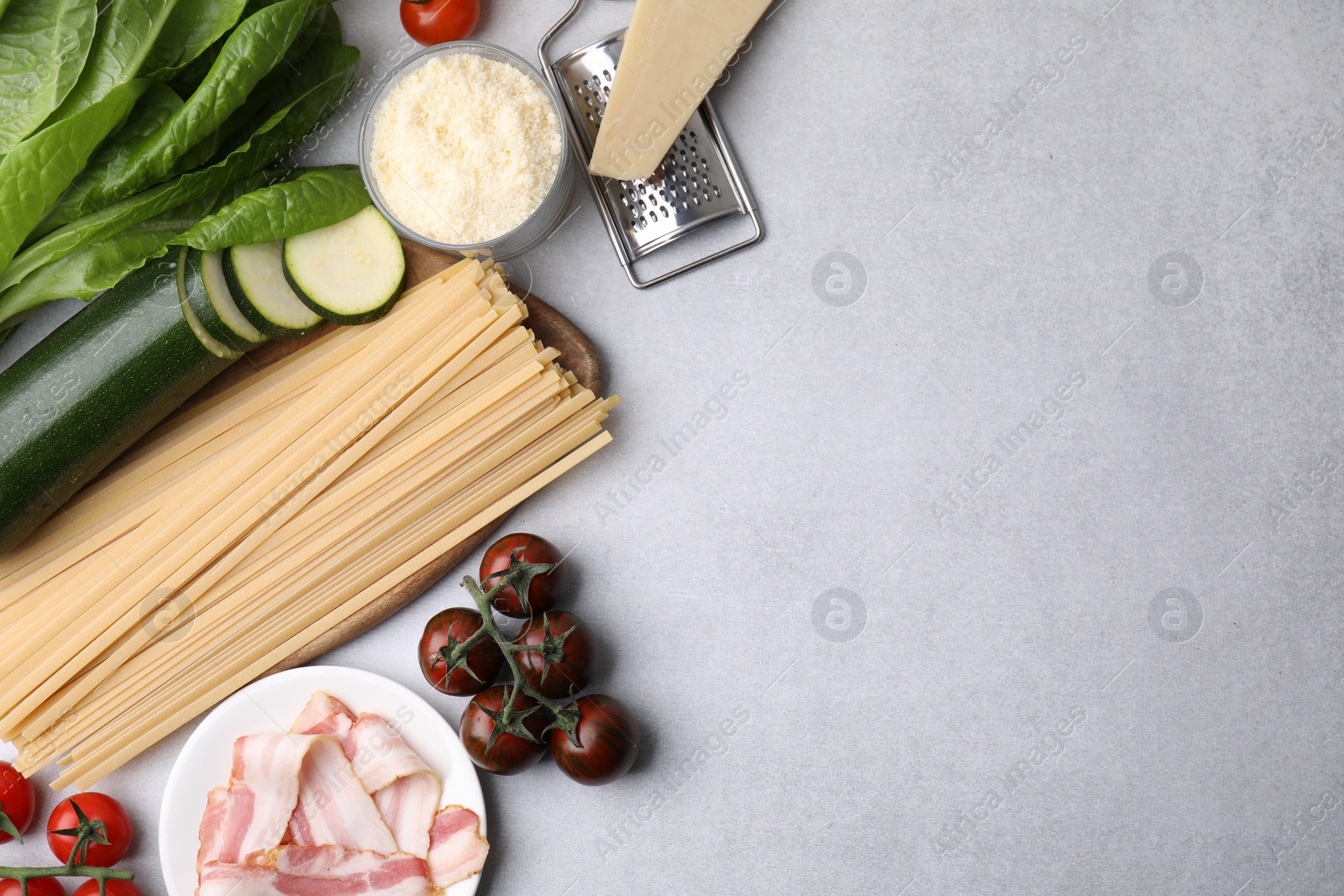 Photo of Raw pasta and fresh ingredients on light grey table, flat lay. Space for text