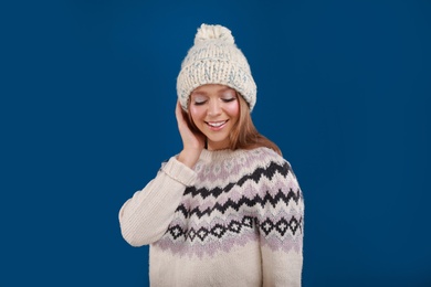 Photo of Young woman in warm sweater and hat on blue background. Winter season