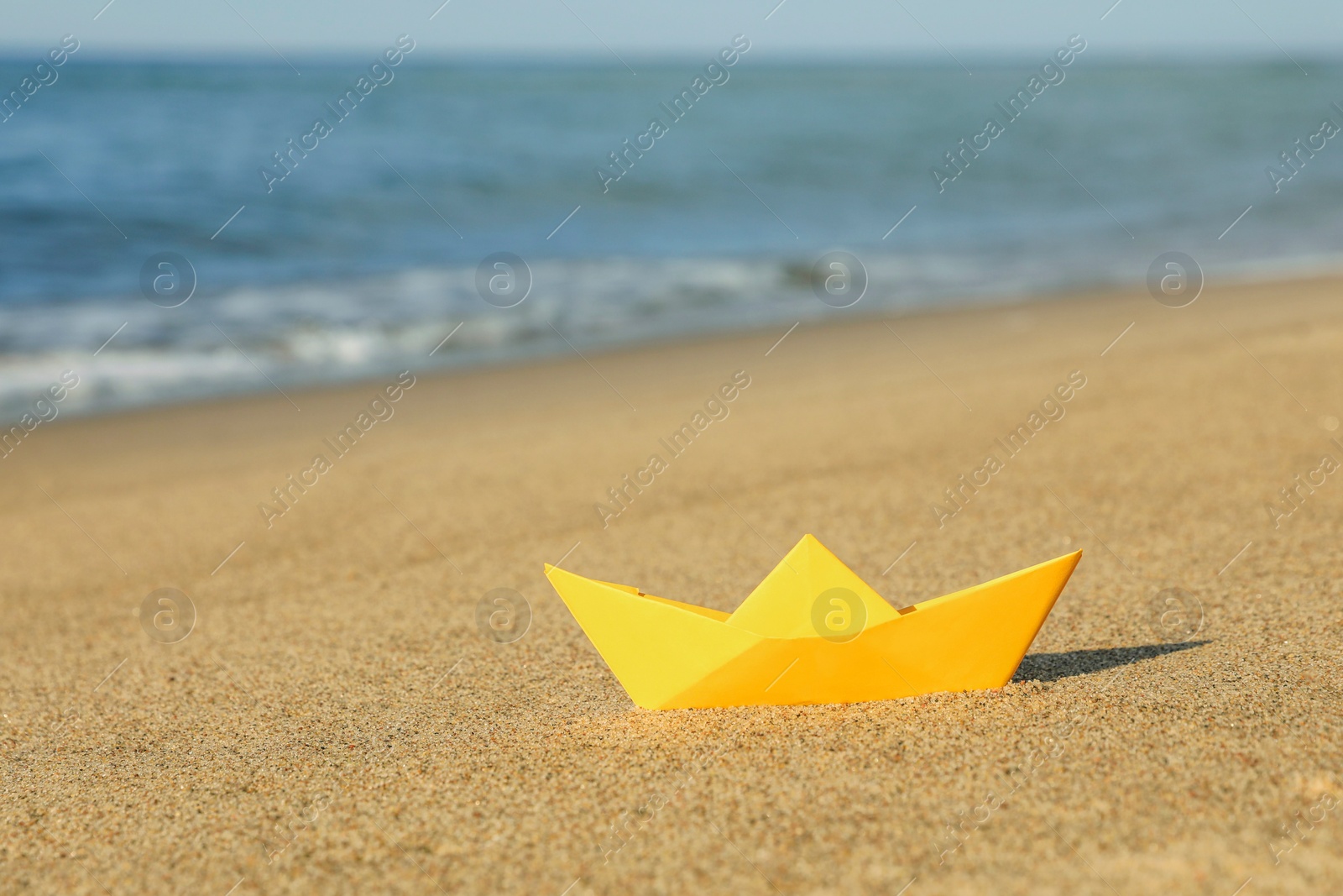 Photo of Yellow paper boat near sea on sandy beach, space for text