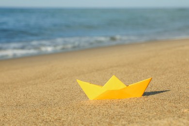 Yellow paper boat near sea on sandy beach, space for text
