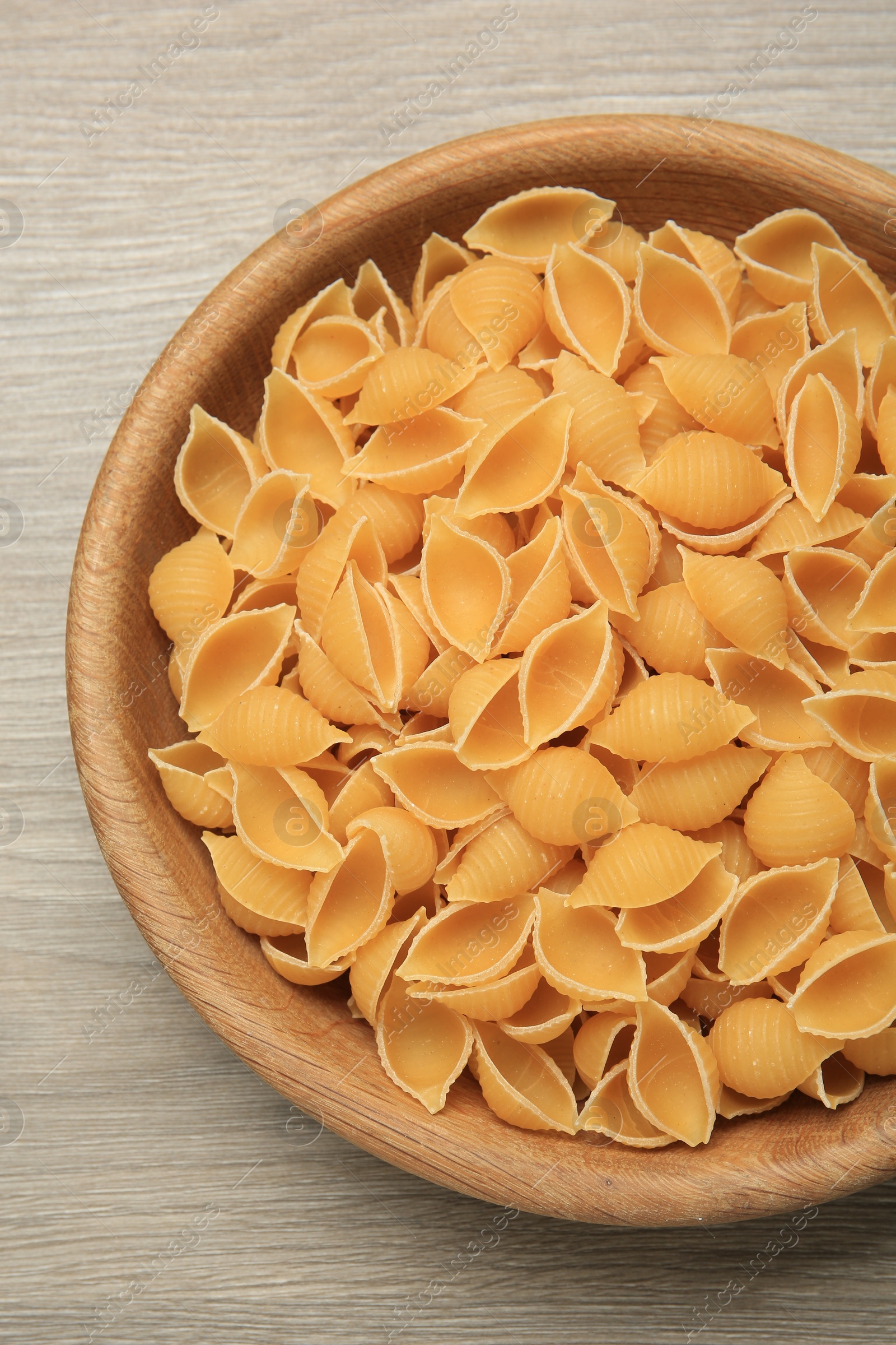 Photo of Raw conchiglie pasta in bowl on light grey wooden table, top view