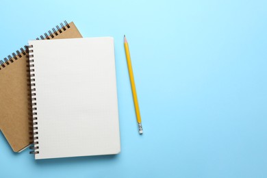 Photo of Notebooks and pencil on light blue background, top view. Space for text