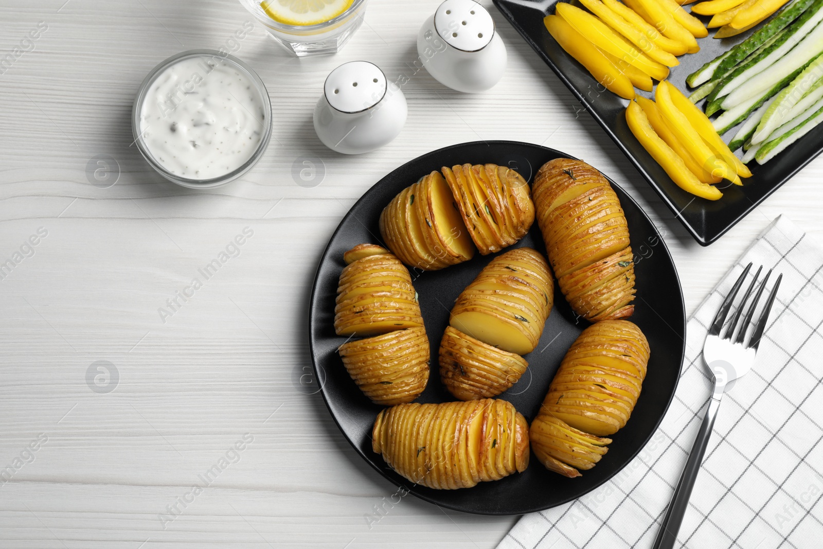 Photo of Delicious homemade Hasselback potatoes served on white wooden table, flat lay. Space for text