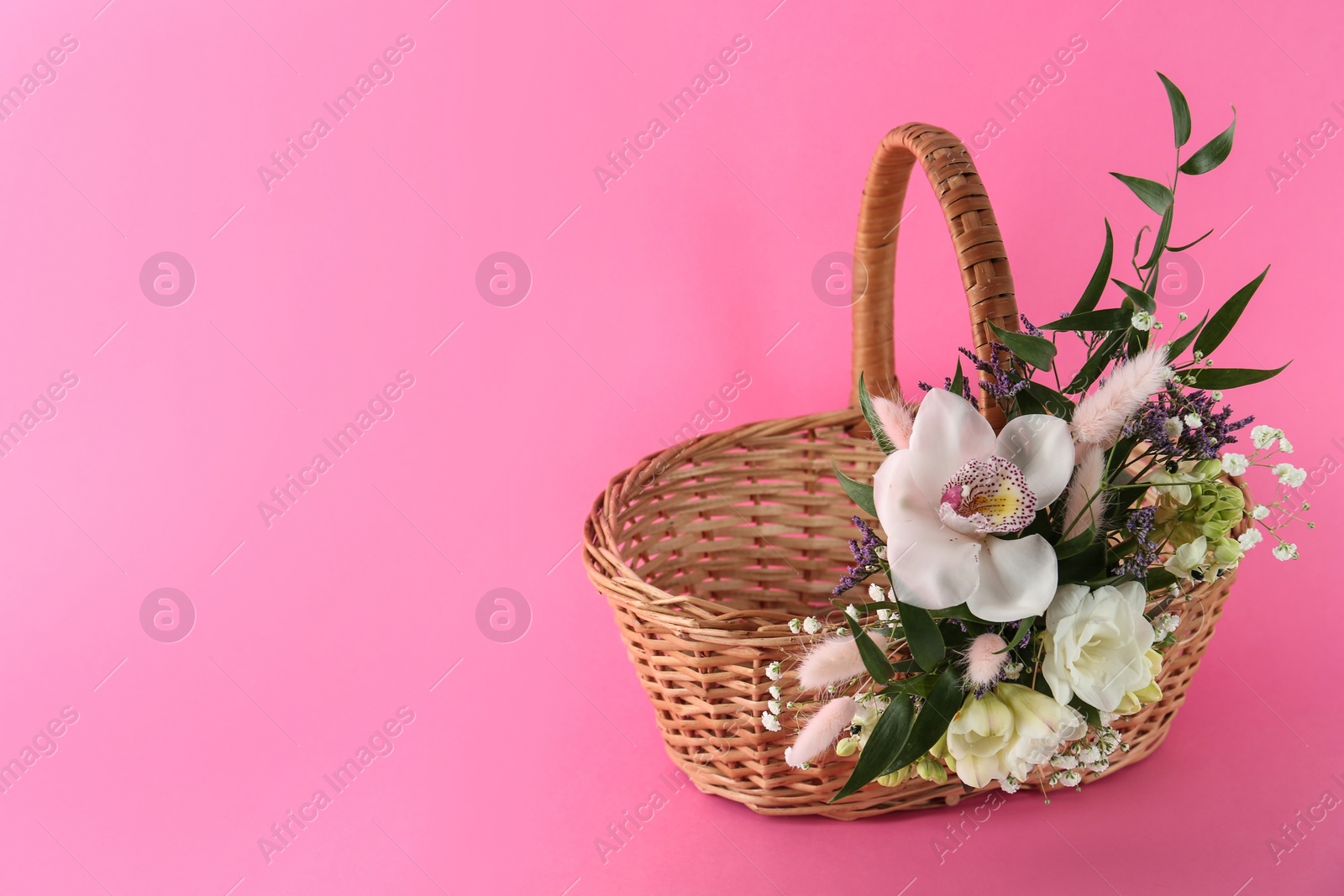 Photo of Wicker basket decorated with beautiful flowers on pink background, space for text. Easter item