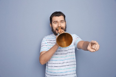 Young man shouting into megaphone on grey background