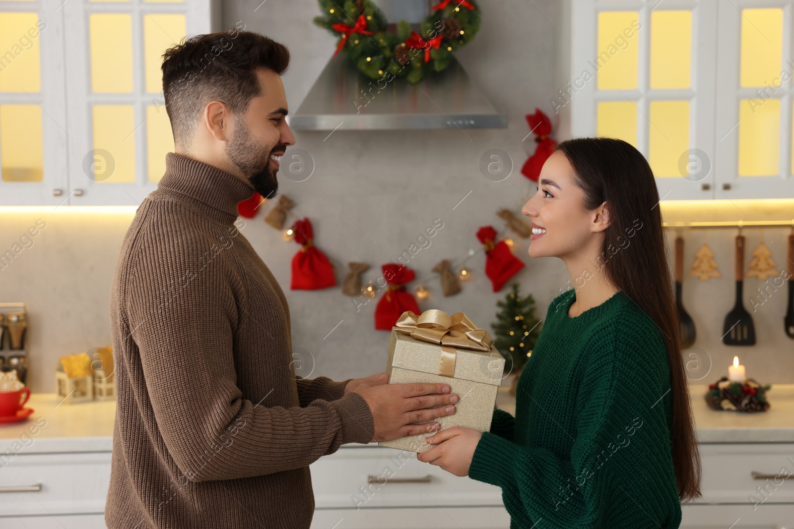 Photo of Happy young man presenting Christmas gift to his girlfriend in kitchen