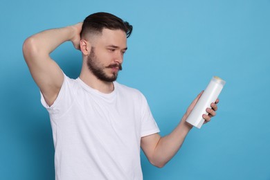 Handsome young man with bottle of shampoo on light blue background