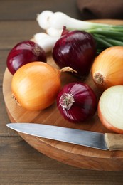 Photo of Board with different kinds of onions on wooden table, closeup