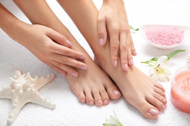 Photo of Cosmetic, flowers and woman touching her smooth feet on white towel, closeup. Spa treatment
