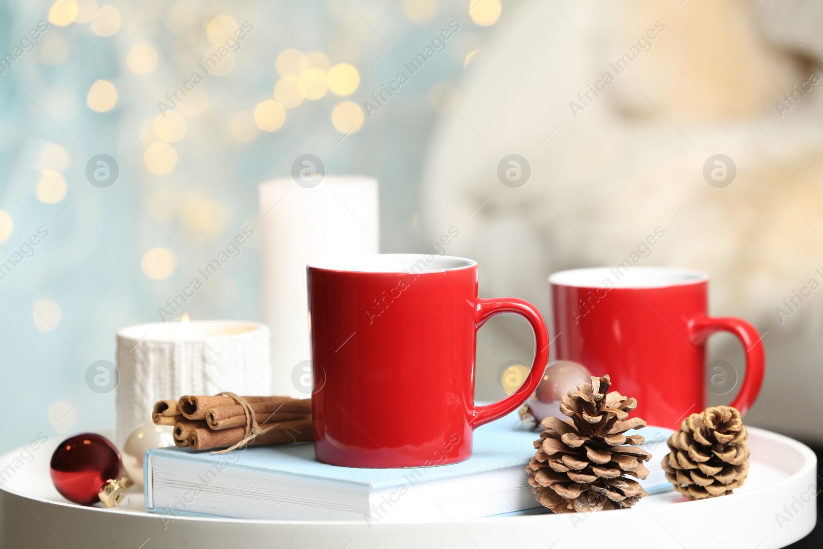 Photo of Cups of hot winter drink and Christmas decoration on white table against blurred lights