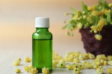 Photo of Bottle of essential oil and linden blossoms on white wooden table, space for text