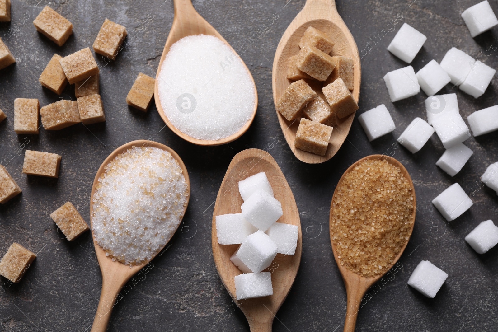 Photo of Spoons with different types of sugar on gray table, flat lay