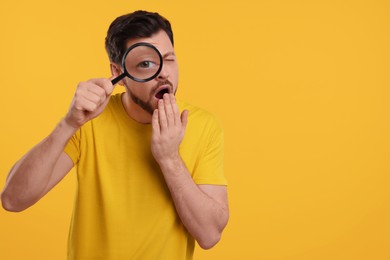Emotional man looking through magnifier glass on yellow background. Space for text