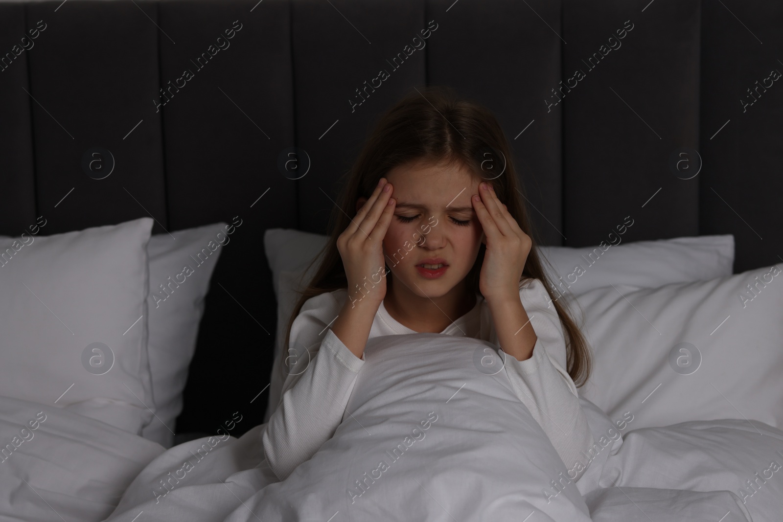 Photo of Little girl suffering from headache in bed at night