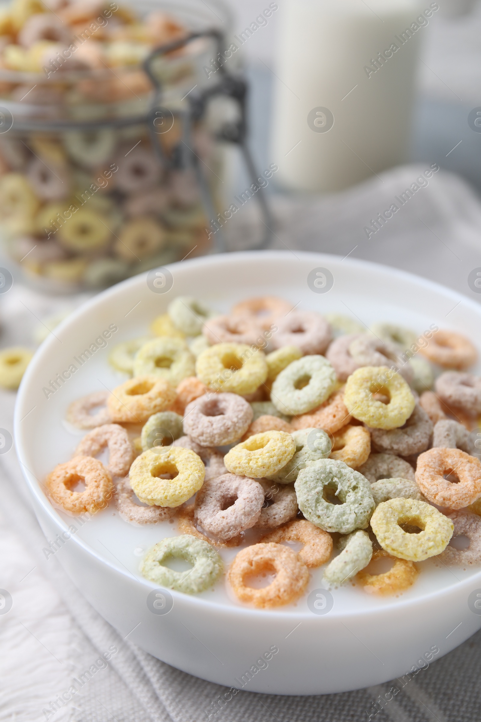 Photo of Tasty colorful cereal rings and milk in bowl on table, closeup