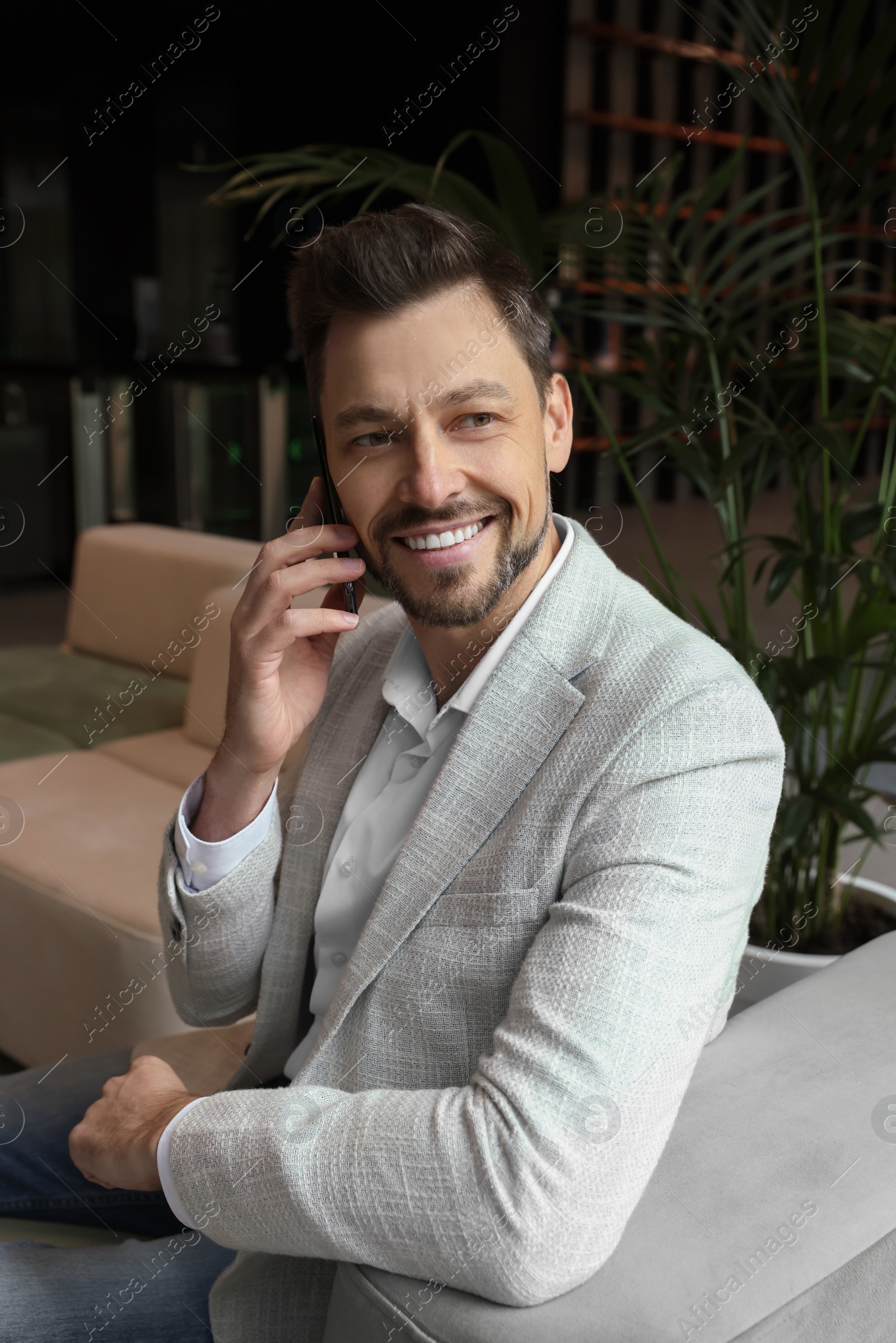 Photo of Attractive happy man sitting and talking on smartphone in hall