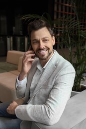 Photo of Attractive happy man sitting and talking on smartphone in hall