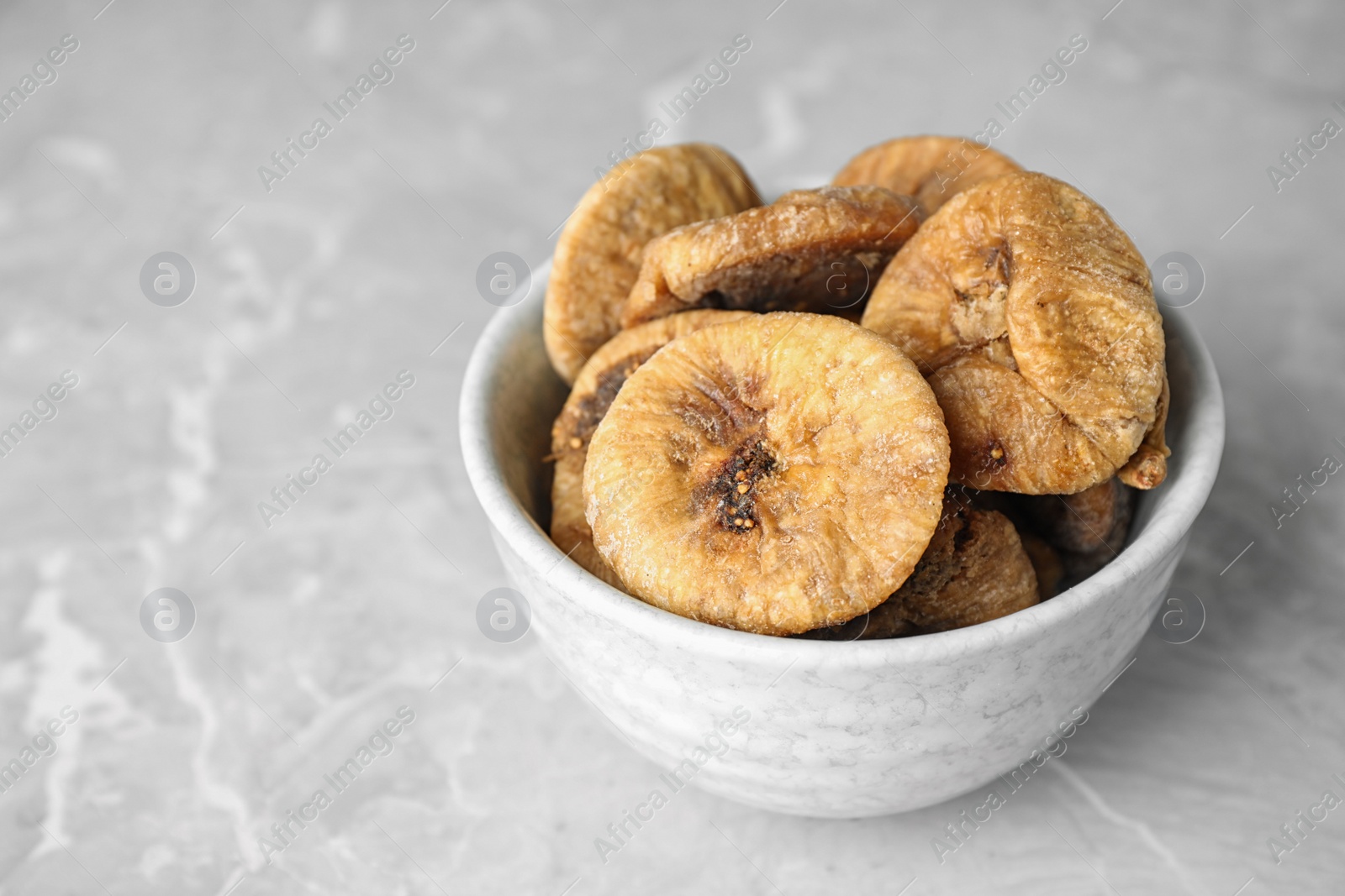 Photo of Bowl of tasty dried figs on light grey marble table, closeup. Space for text