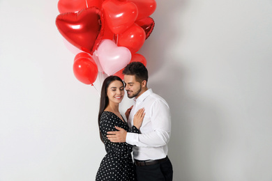 Happy young couple with heart shaped balloons on light background. Valentine's day celebration