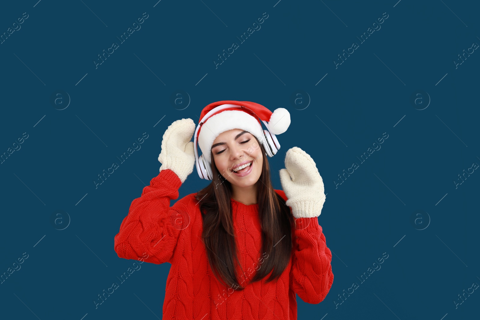 Photo of Young woman in Santa hat listening to Christmas music on dark blue background