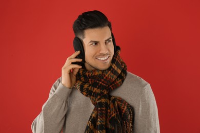 Photo of Man wearing stylish earmuffs and scarf on red background