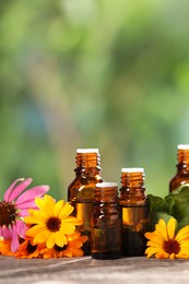 Bottles with essential oils and flowers on wooden table against blurred green background. Space for text