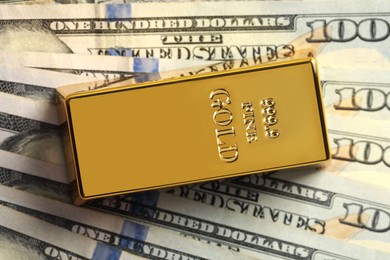 Photo of Shiny gold bar on dollar banknotes, top view