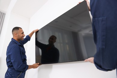 Male movers carrying plasma TV near white wall indoors