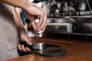 Photo of Barista tamping milled coffee in portafilter at bar counter, closeup. Space for text