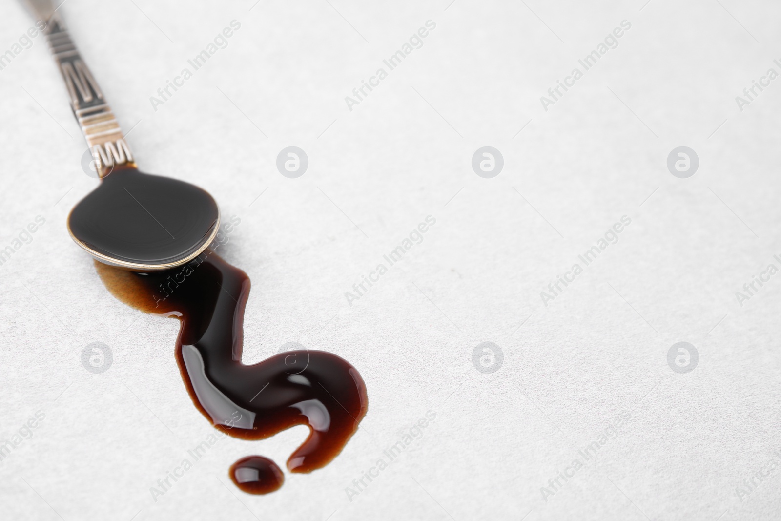 Photo of Spoon with balsamic vinegar on white table, closeup. Space for text