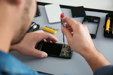 Technician repairing broken smartphone at table, closeup