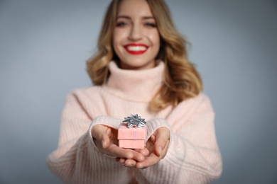 Photo of Young woman with small Christmas gift against grey background, focus on hands