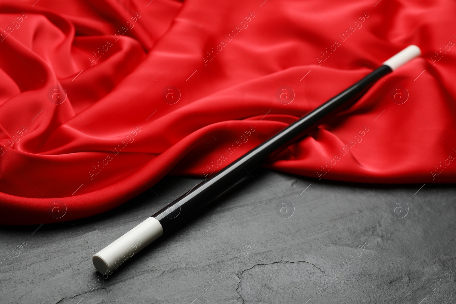 Photo of Beautiful magic wand and red fabric on black table